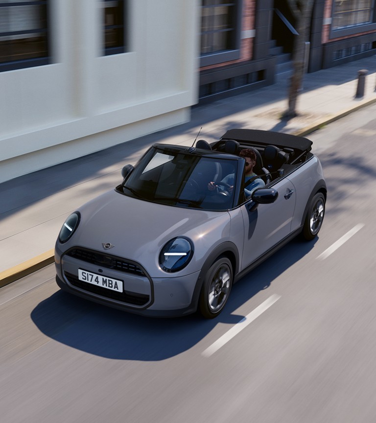 The new MINI convertible is cruising along a road, highlighting its stylish features and open-top design.